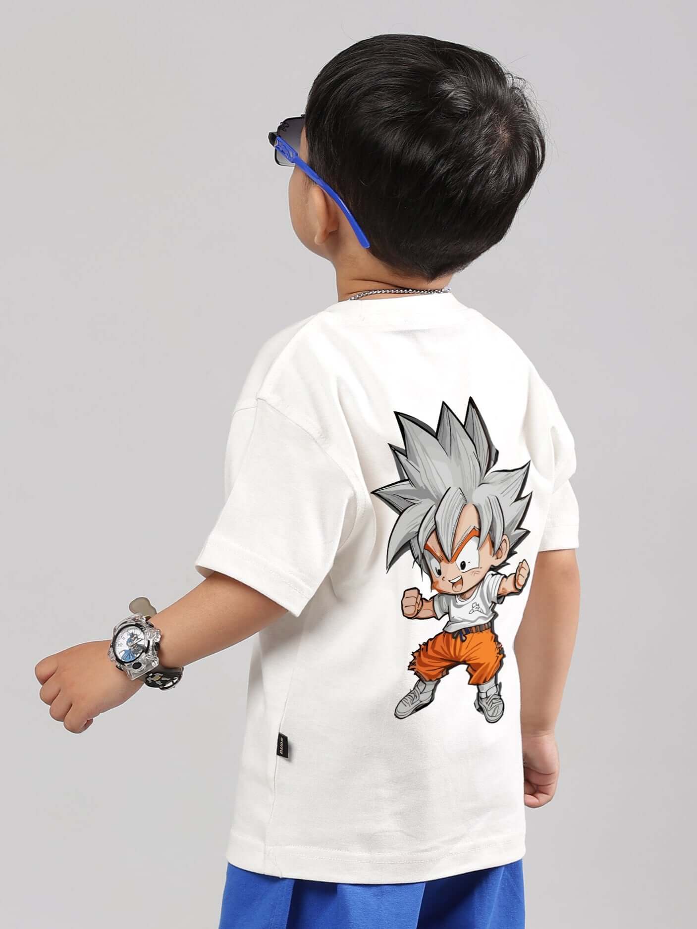 Child wearing off-white GOHAN T-shirt with anime graphic, blue shorts, and sunglasses, showcasing back design. Casual kids fashion.