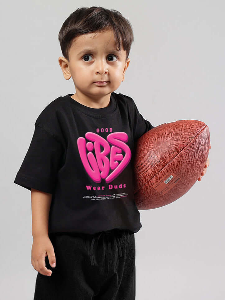 Child wearing a black 'Good Vibes' t-shirt holding a football.