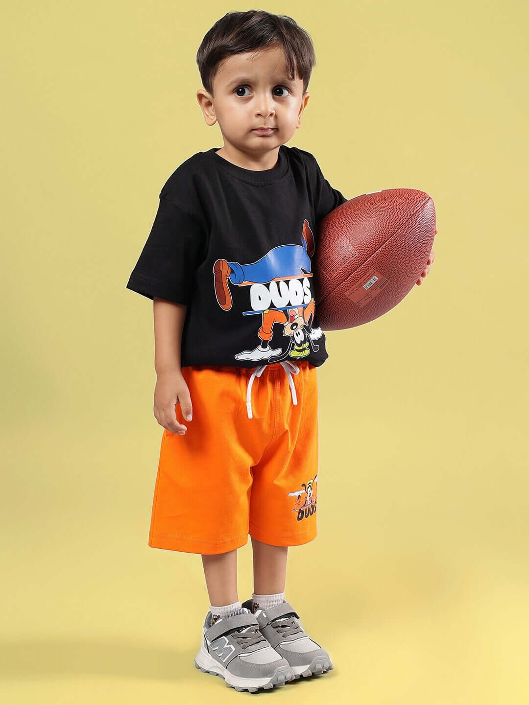 Child wearing GOOFY SUMMER CO-ORD FOR BOYS & GIRLS BLACK-ORANGE holding a football in a stylish outfit, perfect for summer fun.