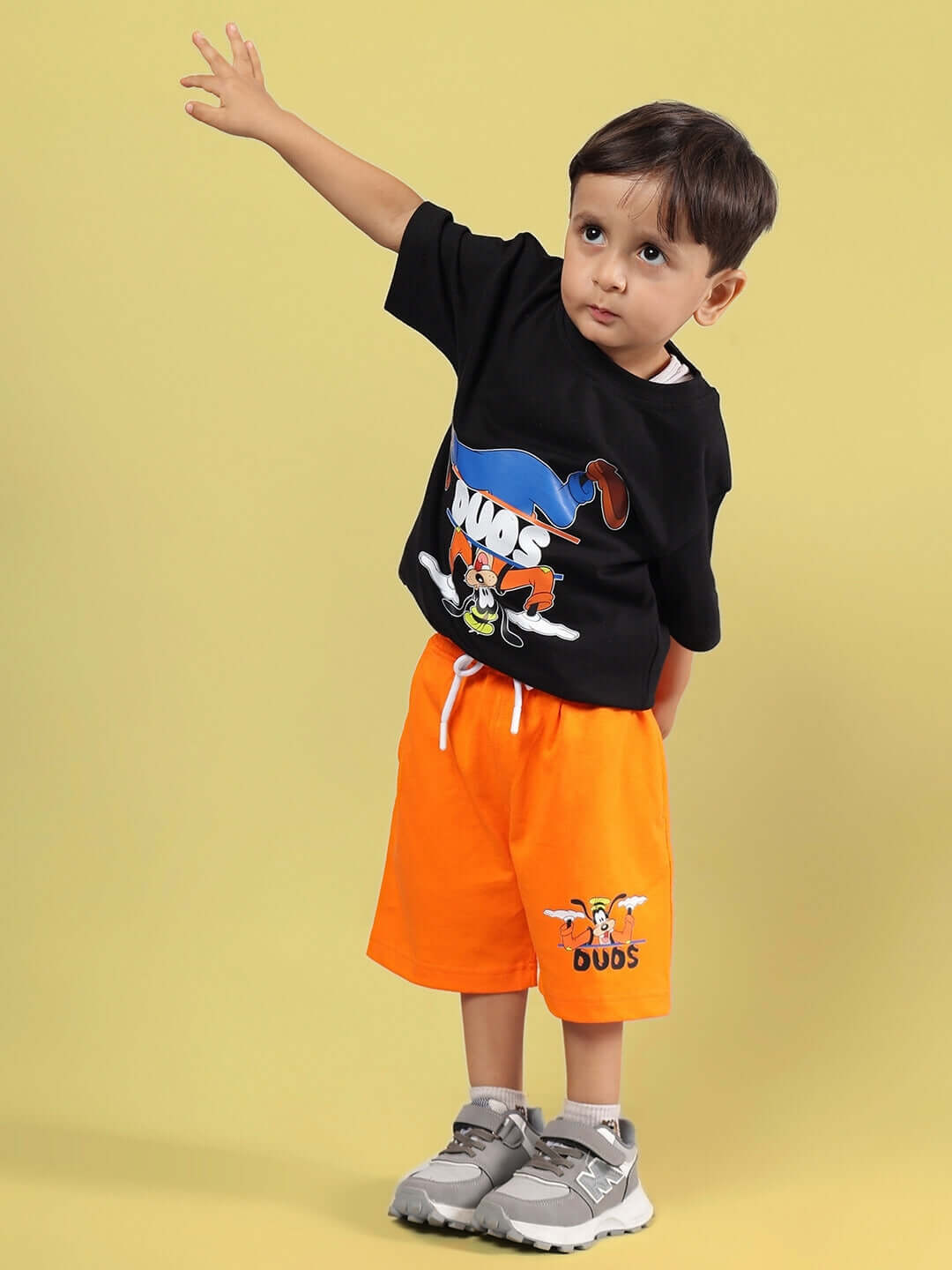 Child wearing GOOFY SUMMER CO-ORD FOR BOYS & GIRLS BLACK-ORANGE with cartoon graphic, featuring black top and orange shorts.