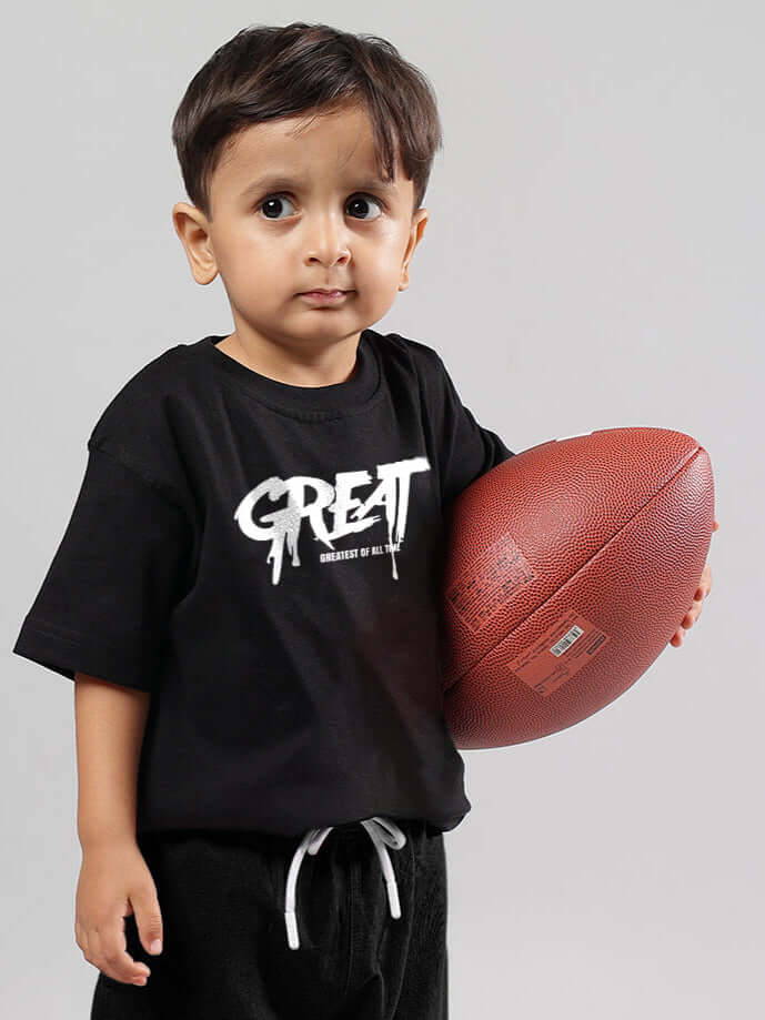 Young child wearing a black oversized printed t-shirt holding a football.