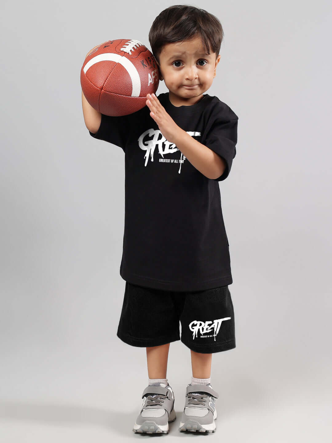 Child in black "Great" printed summer co-ord holding a football, showcasing sporty made-to-order outfit for boys and girls by DUDS.