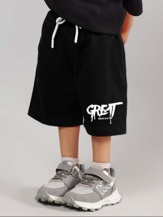 Child wearing black GREAT printed summer shorts with white drawstring and sneakers.
