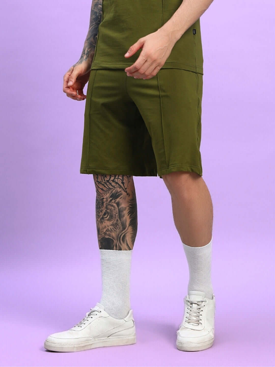 Man wearing Greeble Summer Shorts in olive green with a tattoo, white socks, and sneakers, showcasing style and comfort.