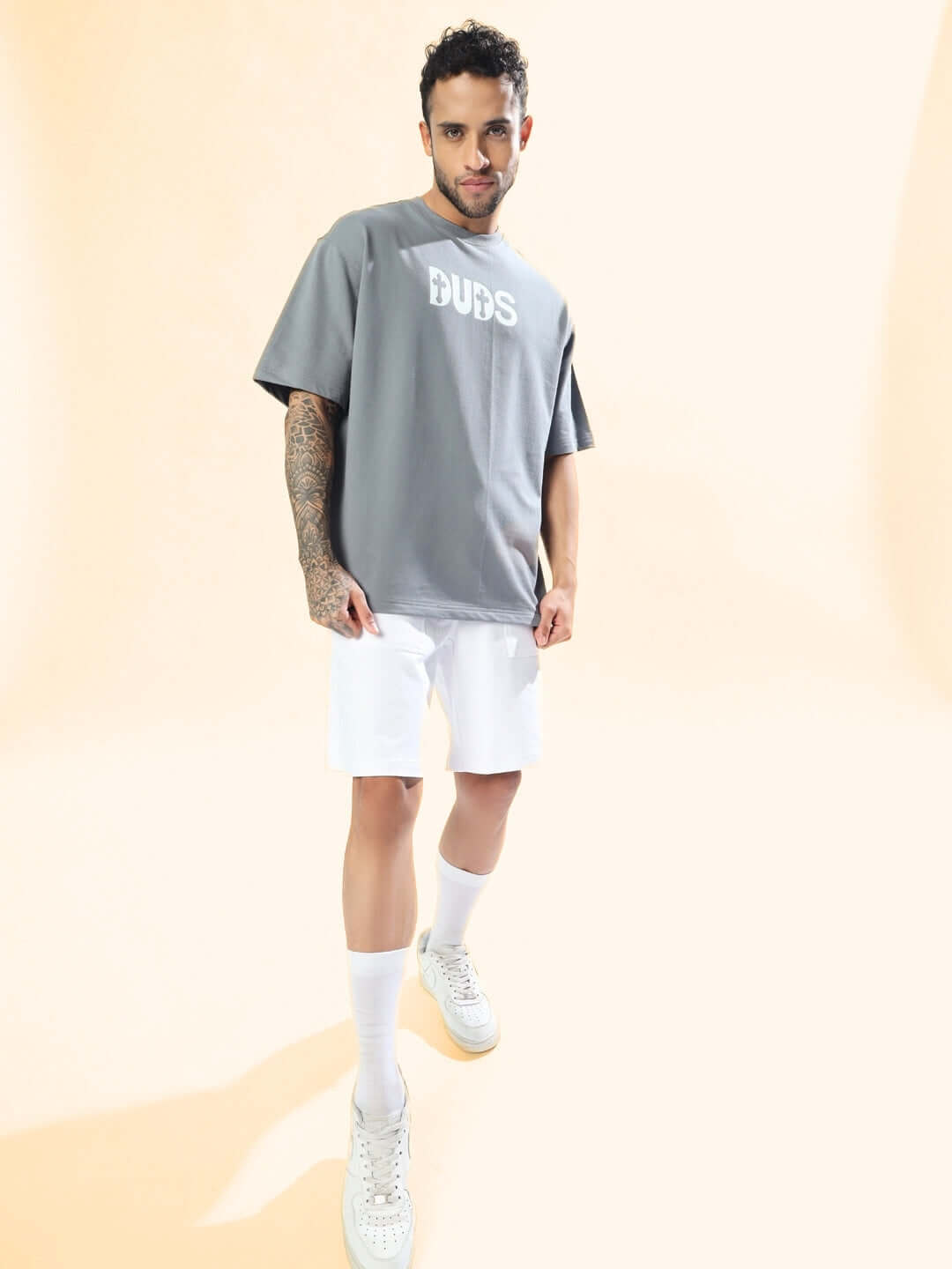 Model wearing 'ONLY GOD CAN JUDGE ME' grey oversized t-shirt with white shorts, showcasing casual style.