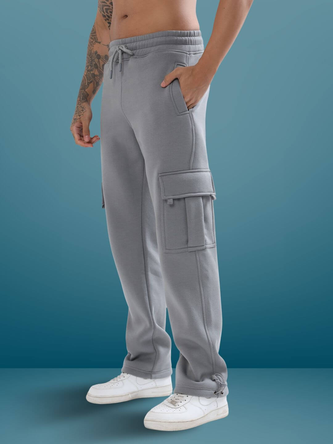 Person wearing grey relaxed fit cargo pants with white sneakers against a blue background.