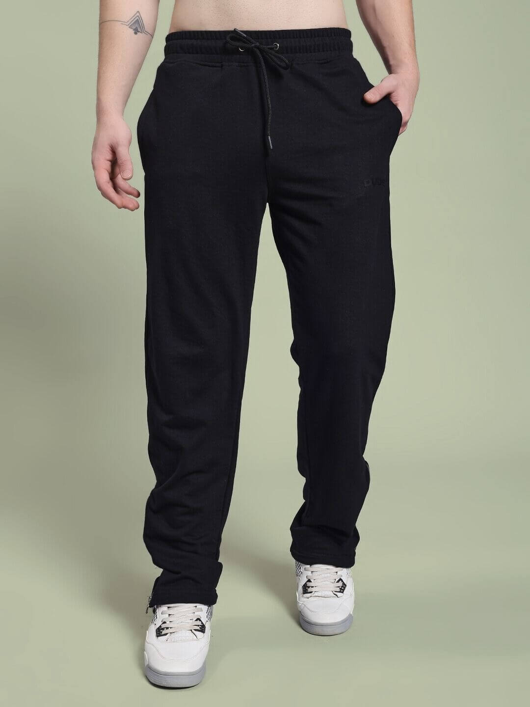 Man wearing JOSS WINS RELAXED-FIT JOGGER BLACK pants with white sneakers on green background.