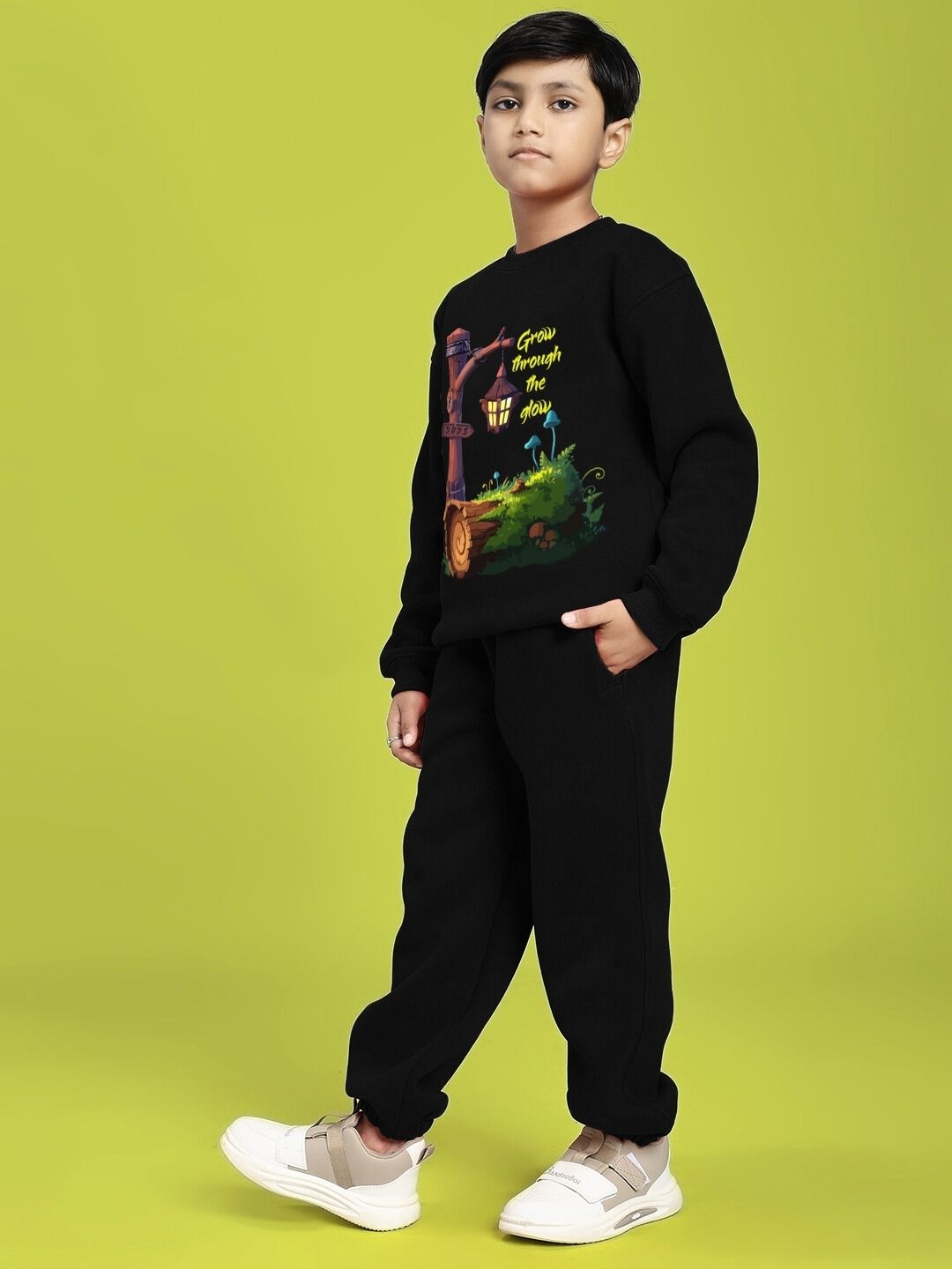 Child wearing GROW AND GLOW PRINT FLEECE CO-ORD FOR BOYS AND GIRLS BLACK standing against a green background