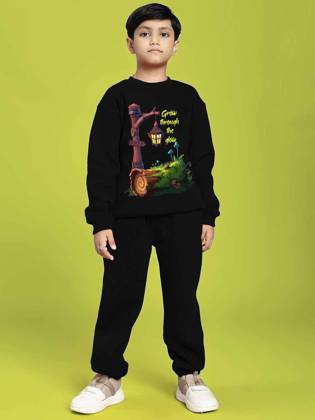 Boy wearing GROW AND GLOW PRINT FLEECE CO-ORD FOR BOYS AND GIRLS BLACK against a green background