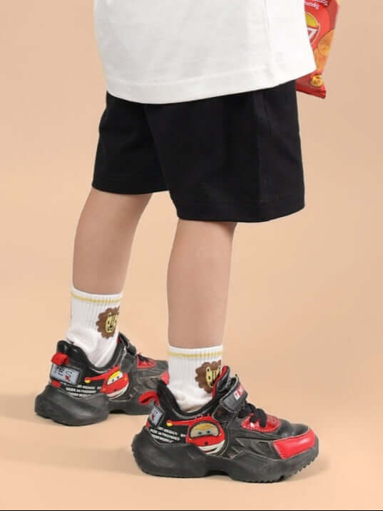 Child wearing HAKUNA MATATA SHORTS FOR BOYS & GIRLS BLACK standing indoors.