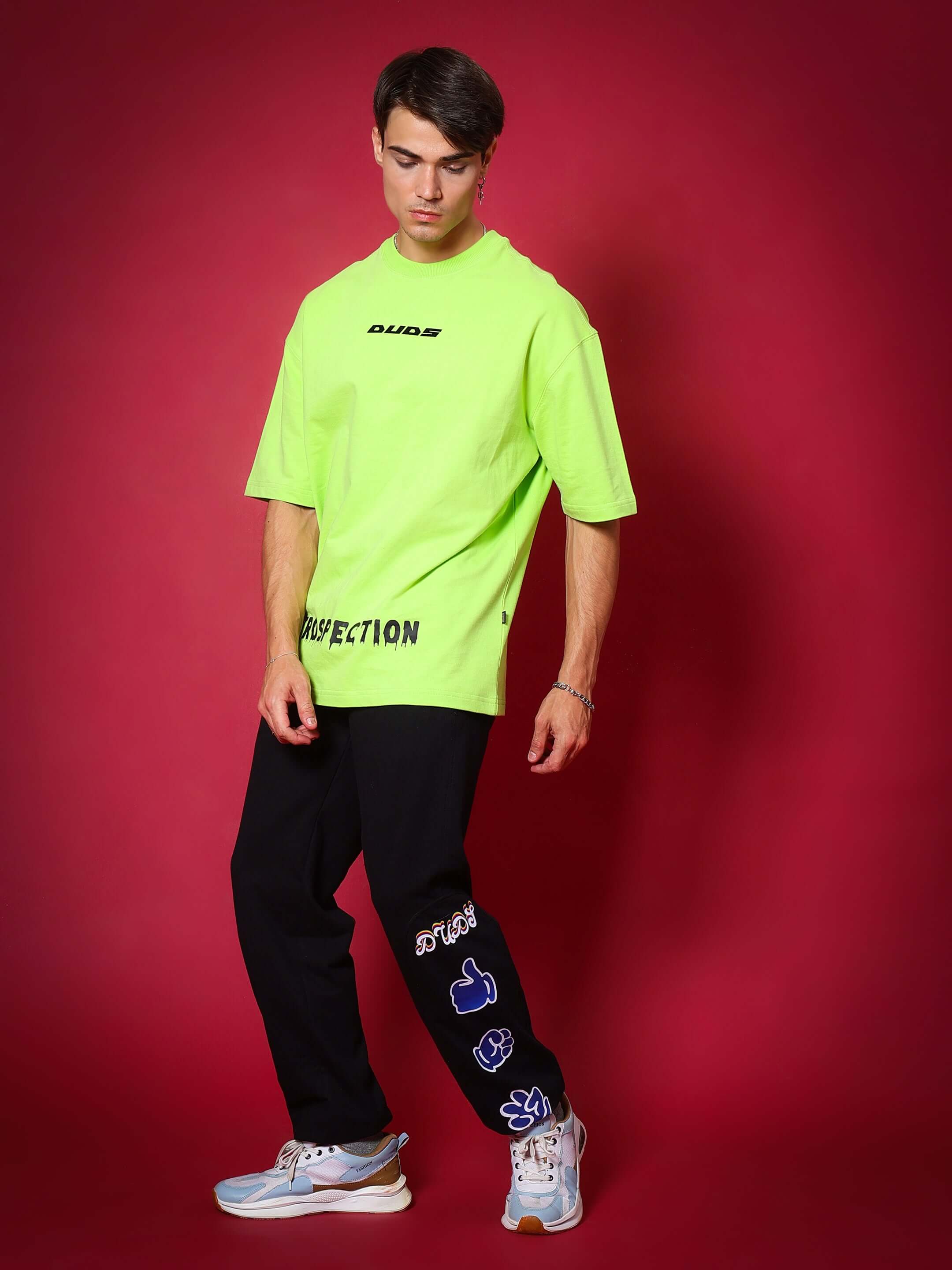 Model wearing HAND GESTURES RELAXED PANT JOGGER in black with neon green t-shirt, showcasing casual streetwear style on a red background.