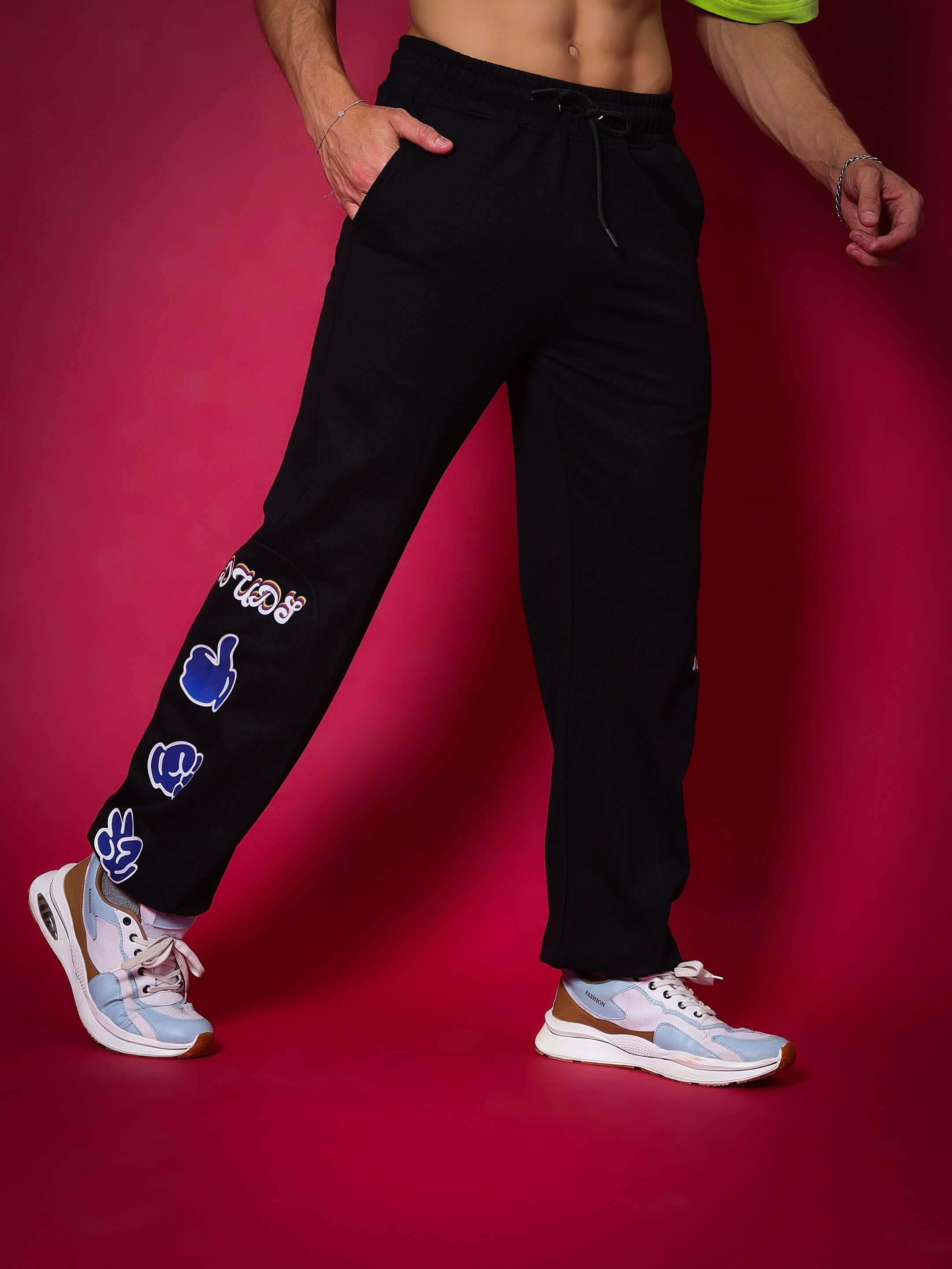 Black relaxed pant jogger with hand gesture designs by DUDS, shown on a model against a red background.