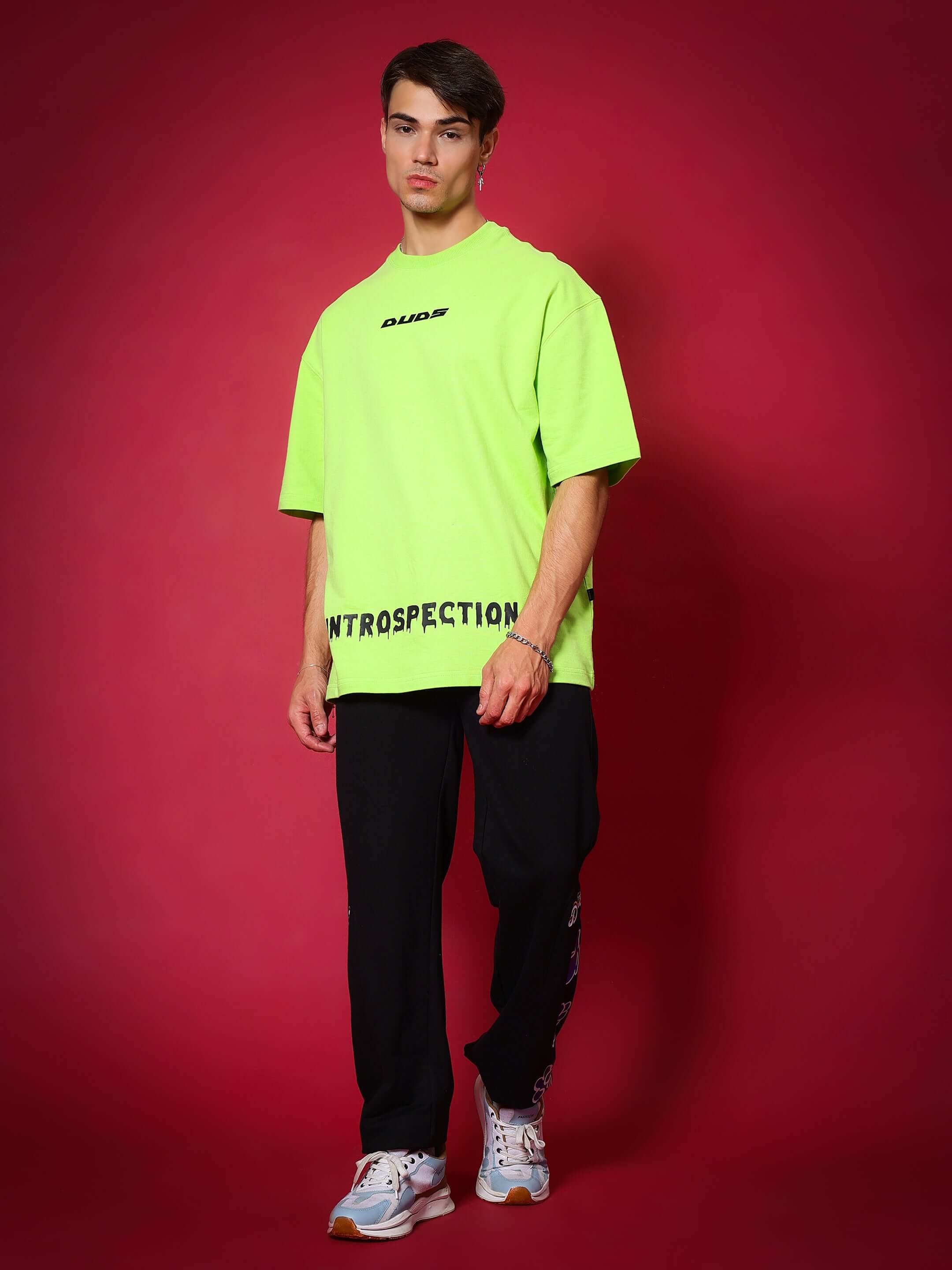 Model wearing black HAND GESTURES RELAXED PANT JOGGER from DUDS with neon green shirt against a red background.