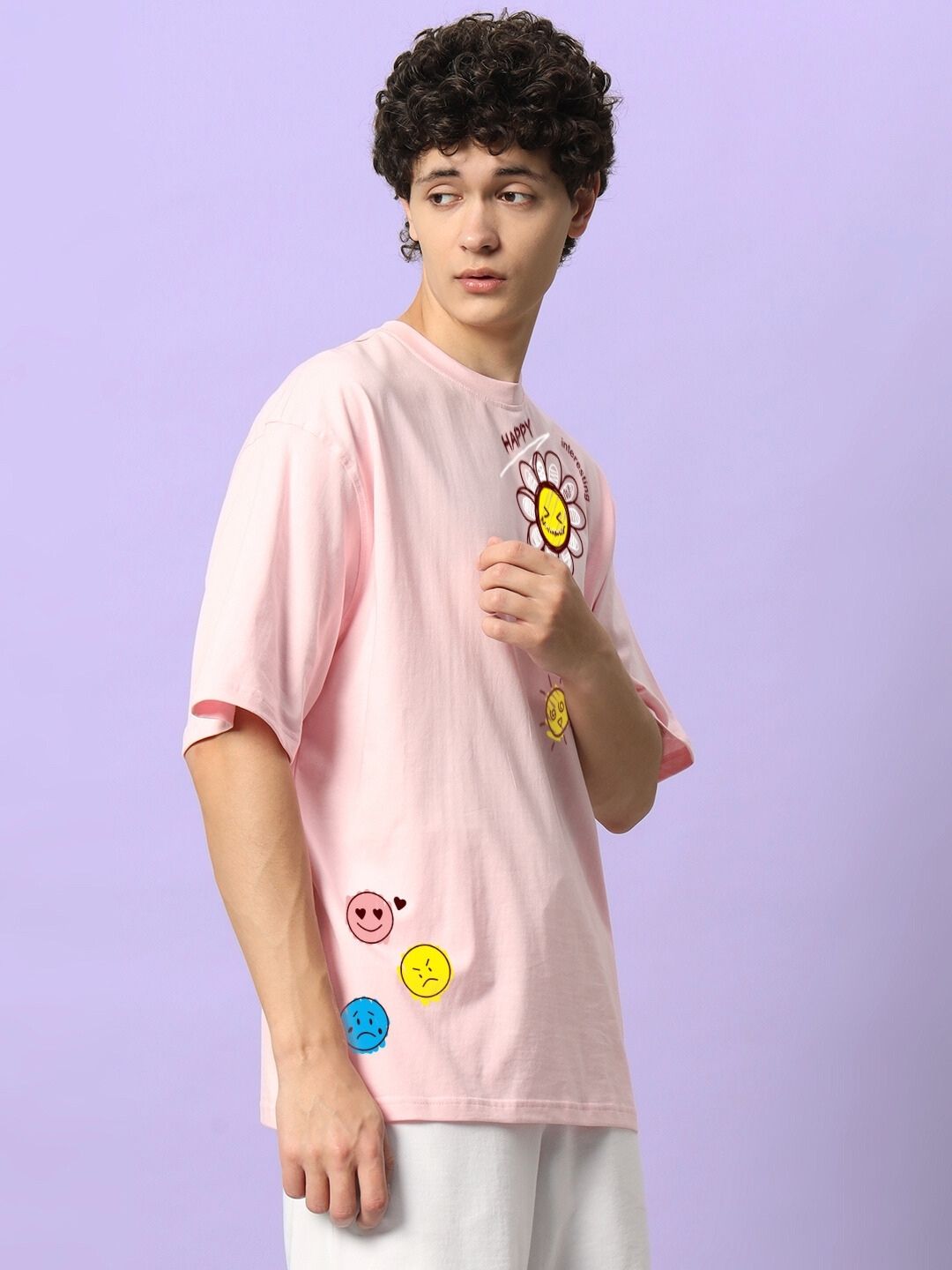 Man wearing HAPPY INTERESTING OVERSIZED T-SHIRT PINK with smiley face graphics, standing against a purple background.