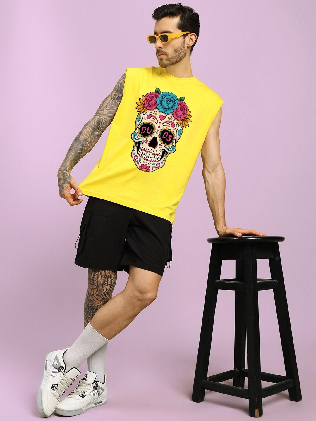 HAPPY SKULL PRINTED GYM T-SHIRT YELLOW worn by a model with black shorts and white sneakers, leaning on a stool, purple background