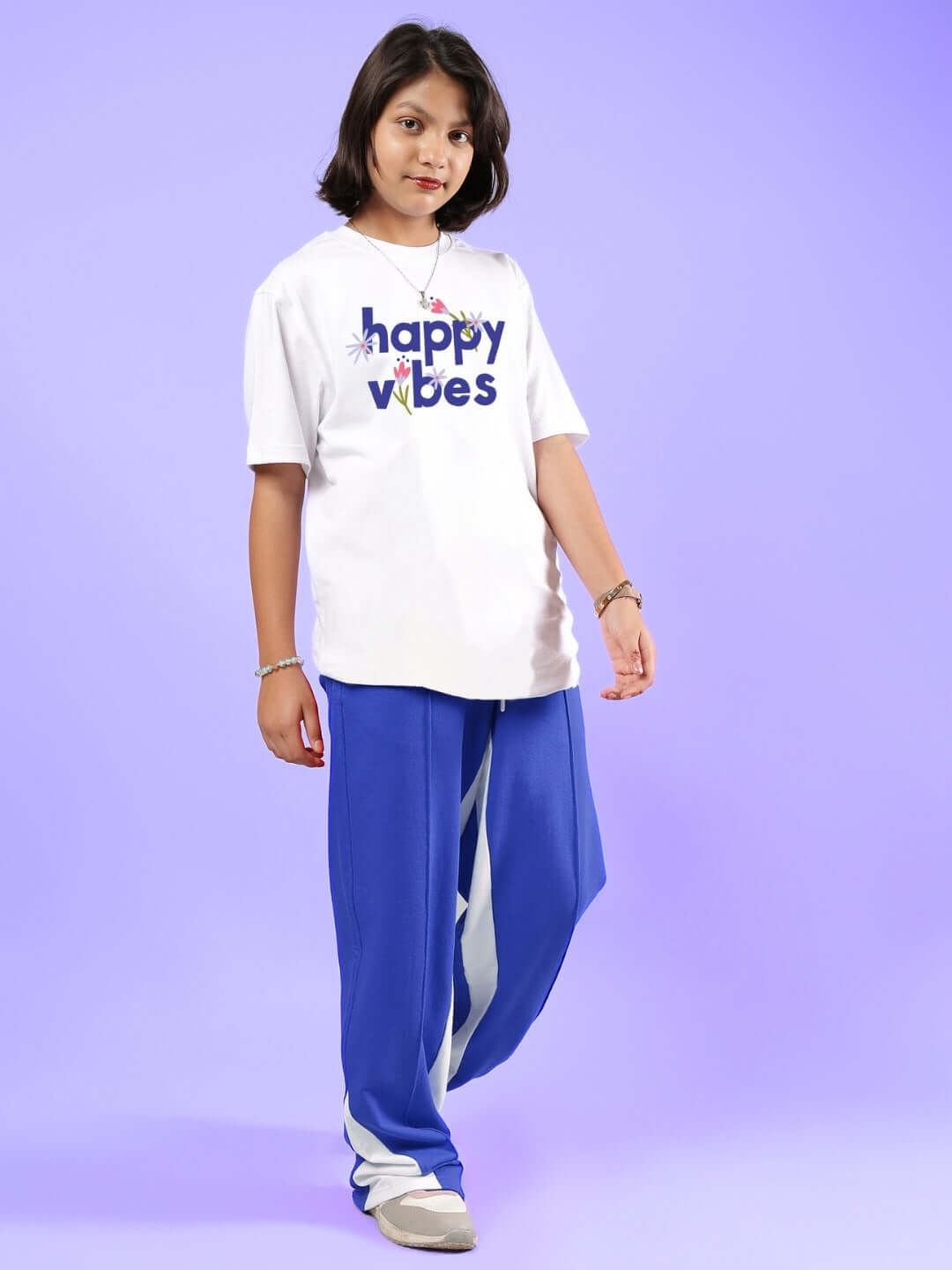 Child wearing Happy Vibes white-blue co-ord set for boys and girls by DUDS, standing against a purple background.