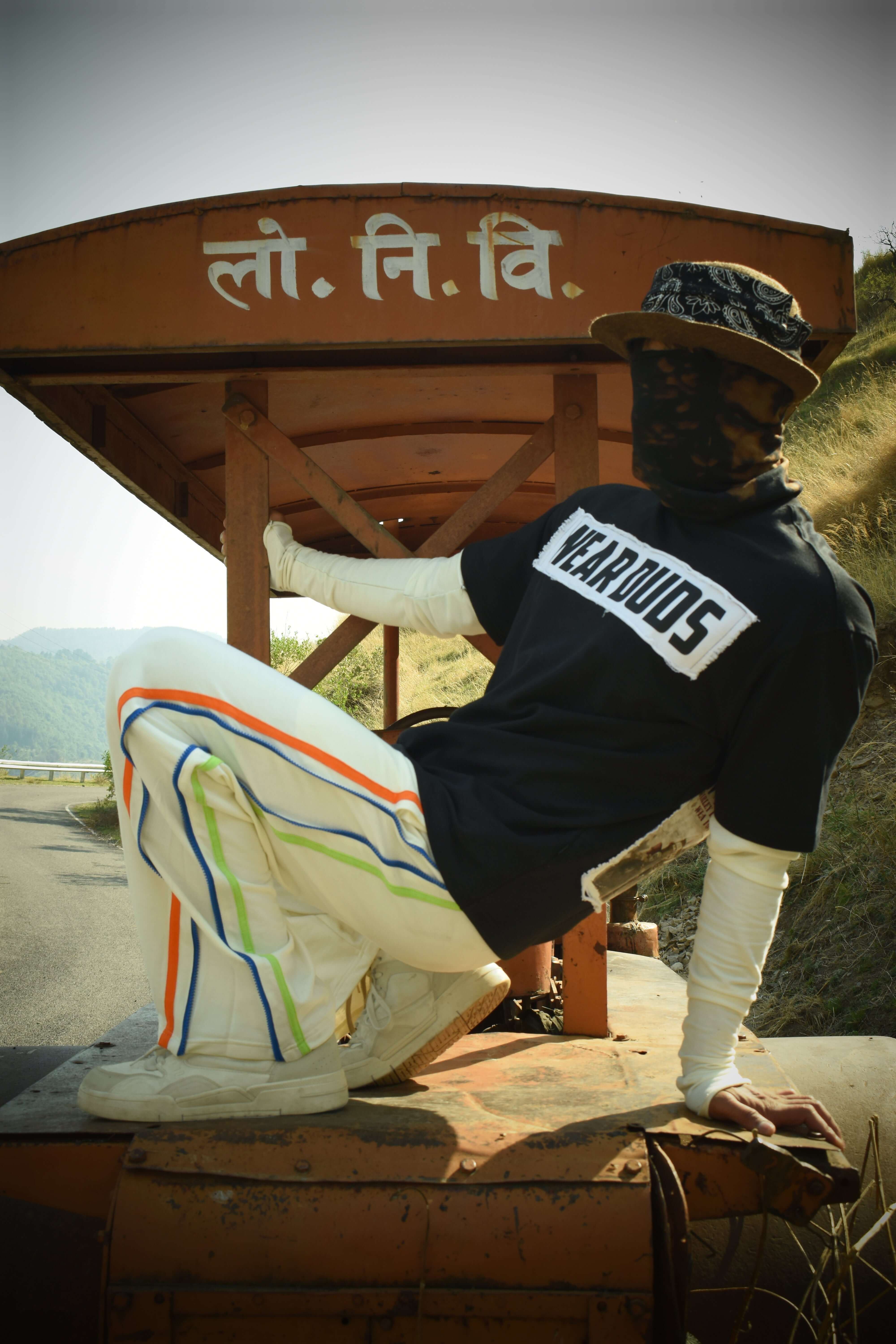 Model wearing black oversized t-shirt with bold graphic, paired with striped pants, in outdoor setting.
