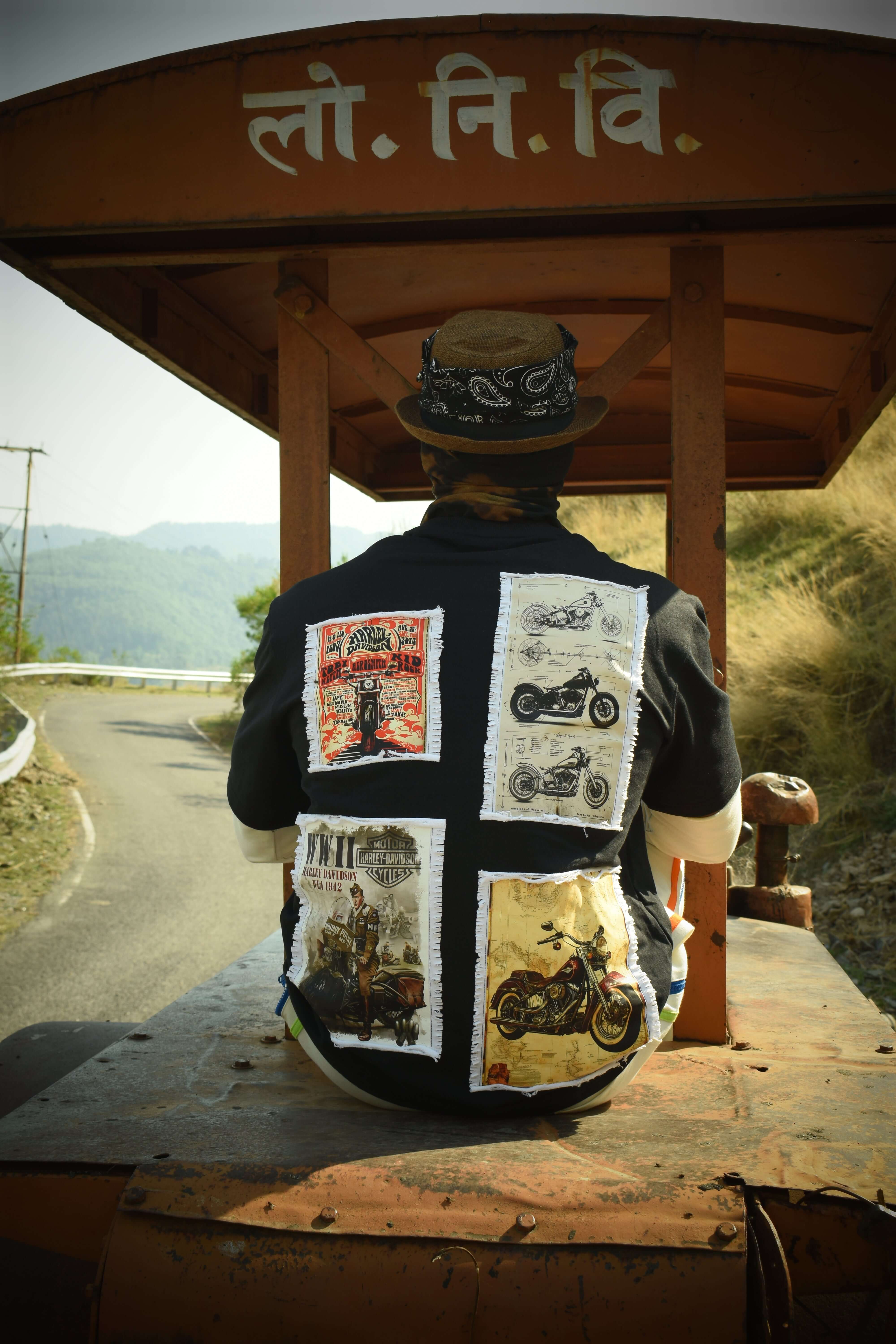 Person wearing a black Harley designer oversized T-shirt with motorcycle patches, sitting on a vintage train in a scenic mountain area.