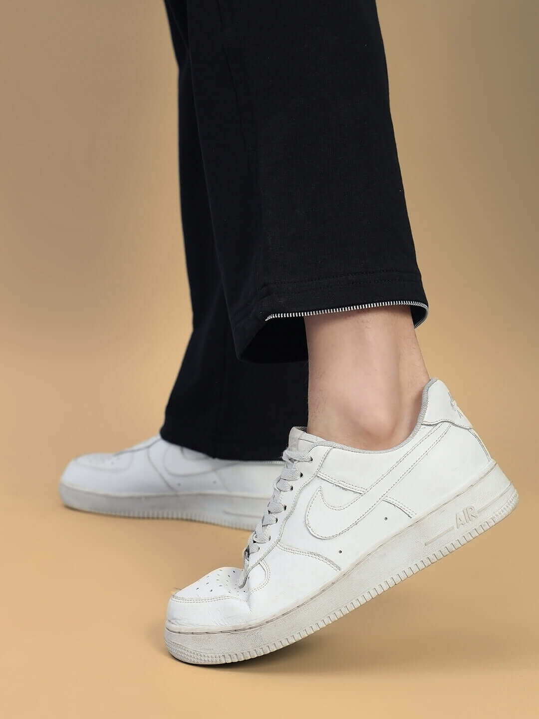 Person wearing white sneakers with black Harper Relaxed Fit Joggers on beige background