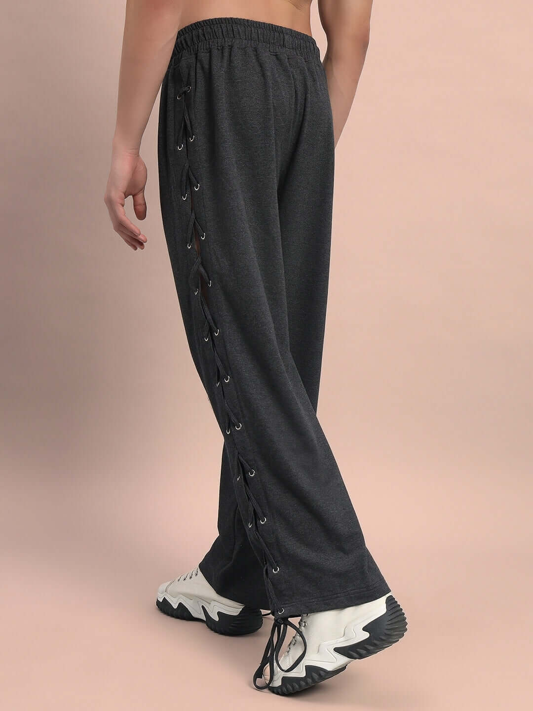 Person wearing grey relaxed fit joggers with side lace-up detail, paired with white sneakers, against a neutral background.