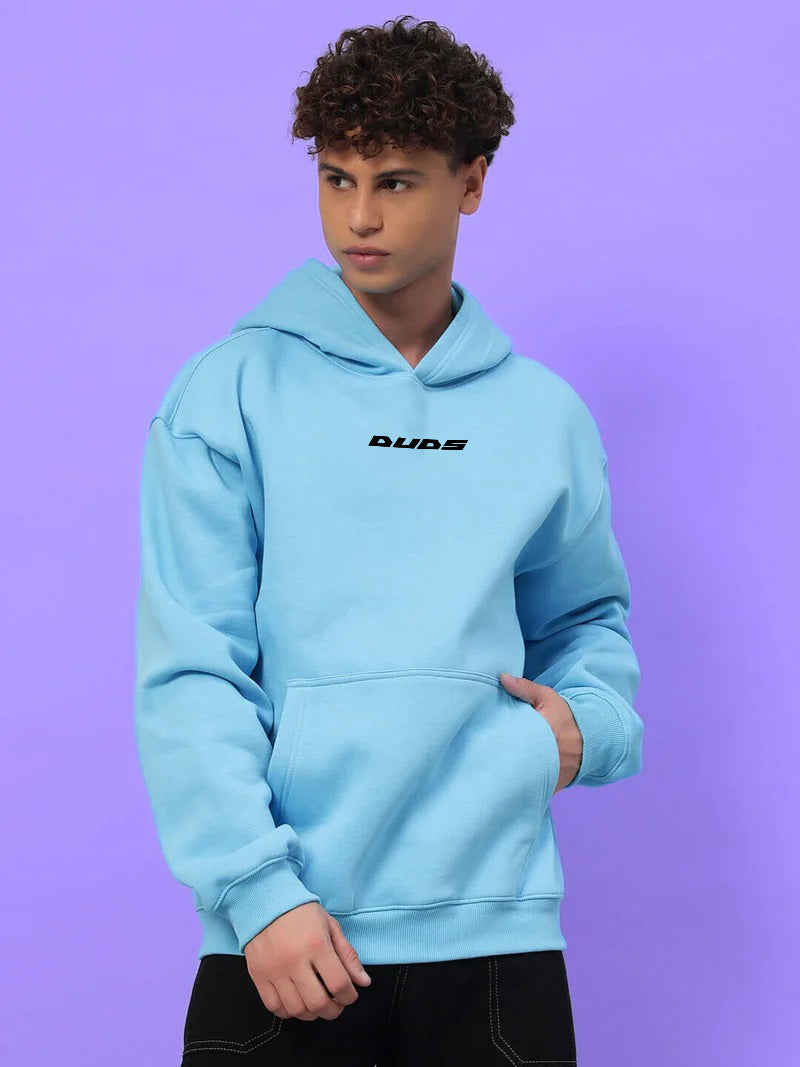 Man wearing HEARTBREAK OVERSIZED FLEECE HOODIE LIGHT BLUE in a casual style against a purple background.