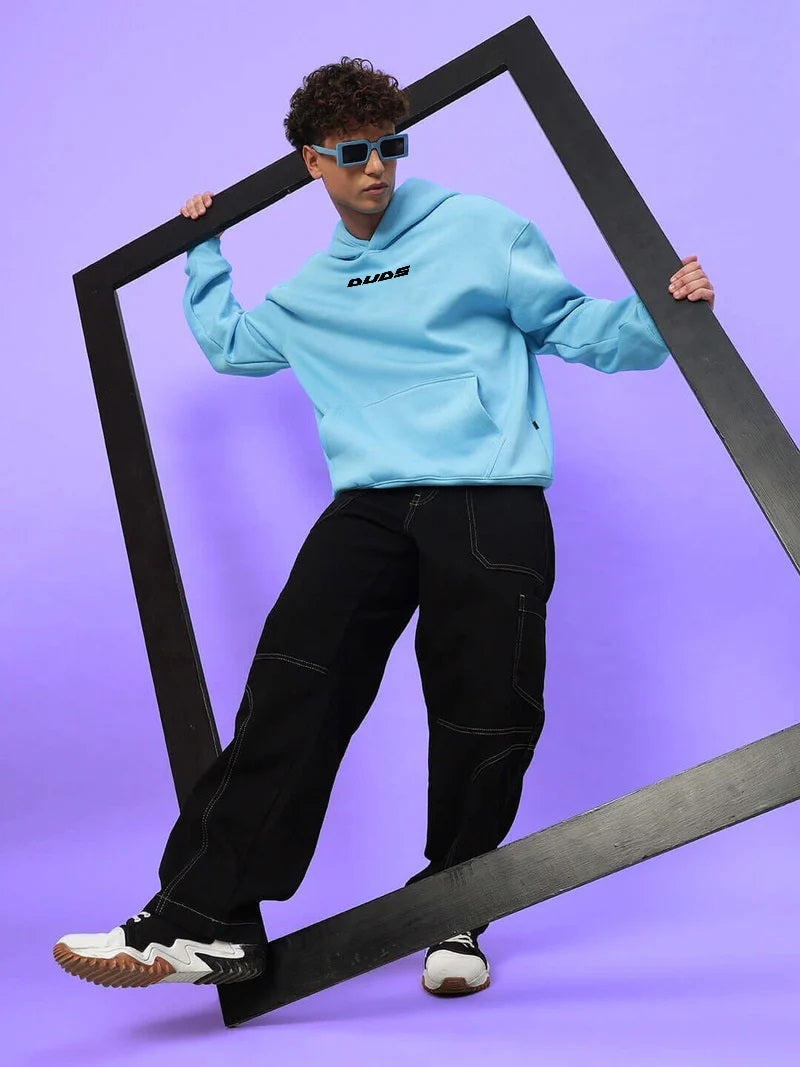 Stylish model wearing HEARTBREAK OVERSIZED FLEECE HOODIE LIGHT BLUE with black pants and sneakers, showcasing modern streetwear fashion.