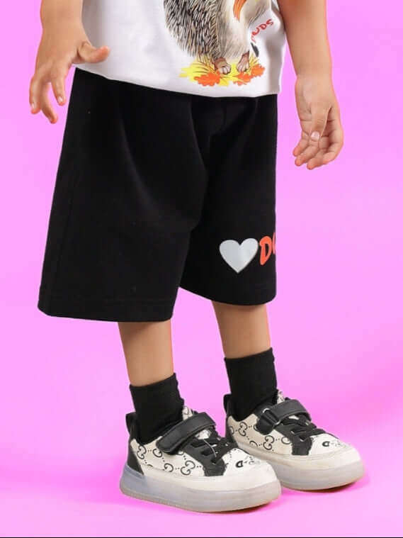 HEDGEHOG SHORTS FOR BOYS & GIRLS BLACK modeled by a child with sneakers on a pink background