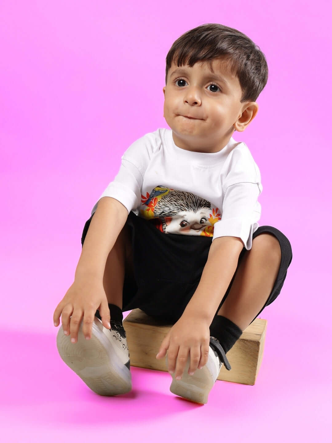 Child wearing HEDGEHOG SHORTS FOR BOYS & GIRLS BLACK sitting on a block, showcasing playful design and comfortable fit.