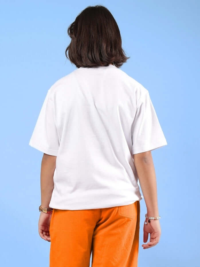 Rear view of child wearing HELLO SPRING T-SHIRT FOR BOYS & GIRLS WHITE paired with orange pants, standing against a blue background.