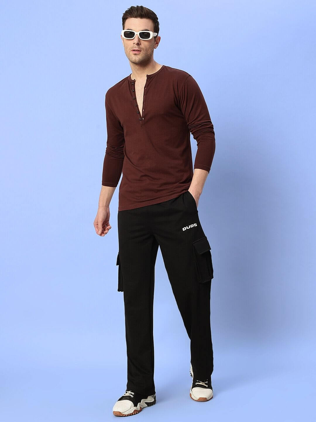 Model wearing HENNY RELAXED FIT CO-ORD SET BROWN-BLACK, consisting of a brown top and black pants, against a blue background.