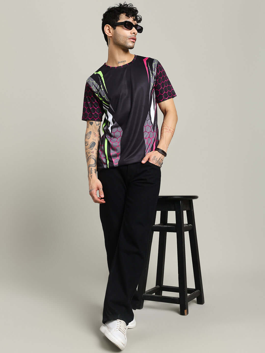 Man wearing black HEXAGON PRINTED REGULAR FIT T-SHIRT BLACK with colorful patterns, standing against neutral background.