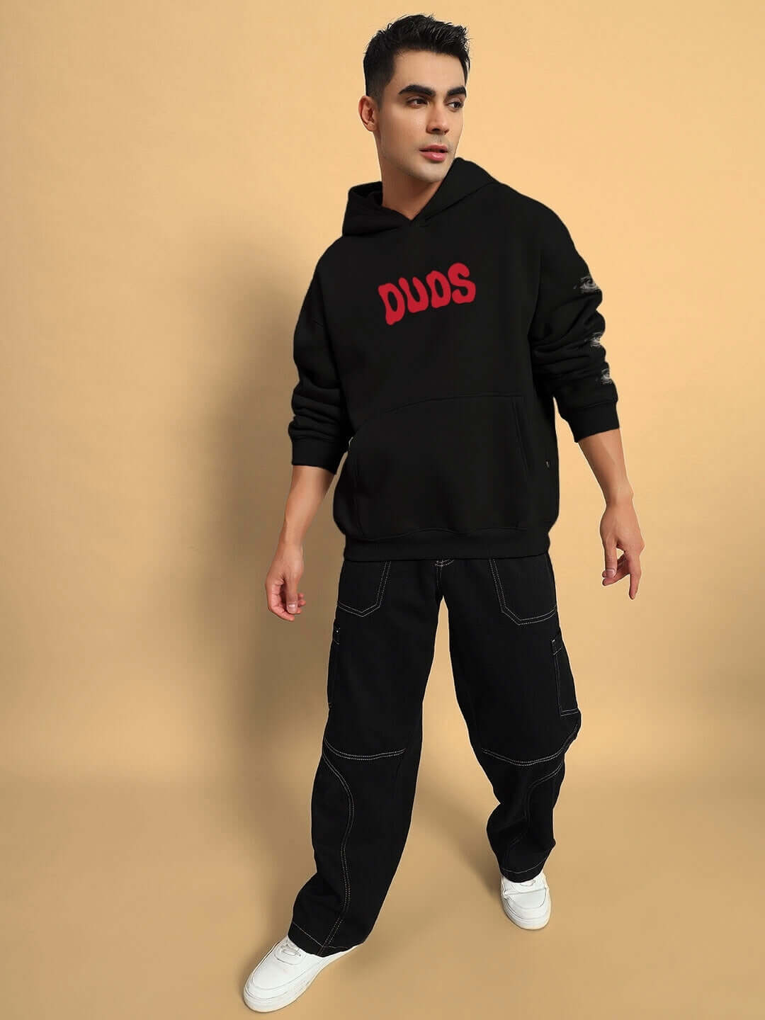 Person wearing Hidden World oversized black fleece hoodie with red text on the front, paired with dark jeans and white sneakers.