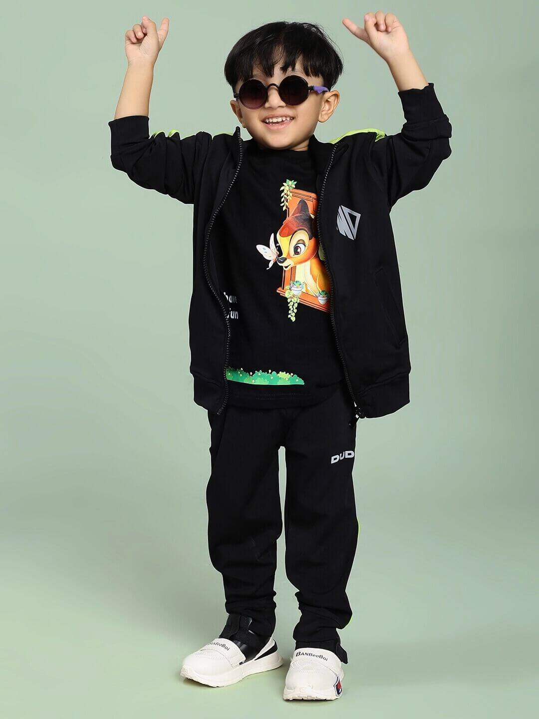 Child in a HIGH PERFORMANCE JACKET FOR BOYS AND GIRLS BLACK, wearing sunglasses, raises arms in playful pose, showcasing the stylish jacket.