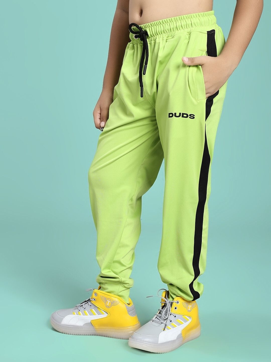 Child wearing HIGH PERFORMANCE JOGGER FOR BOYS AND GIRLS NEON GREEN with yellow sneakers, showcasing comfortable athletic fit.