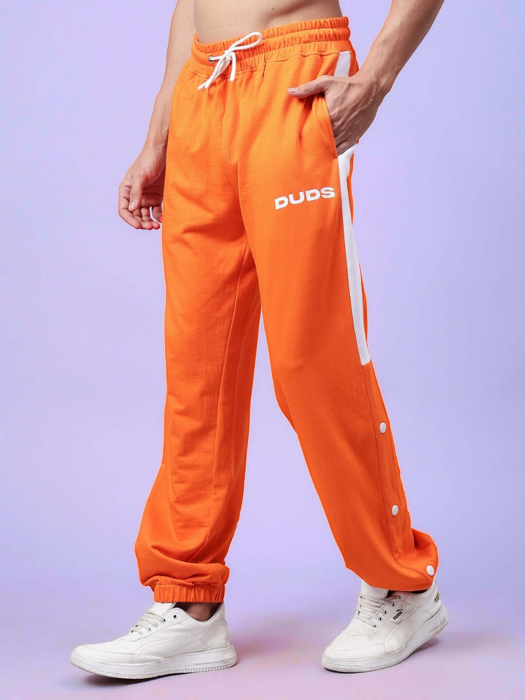 Model wearing orange-white DUDS High Point Contrast Joggers with customizable size options, standing in white sneakers.