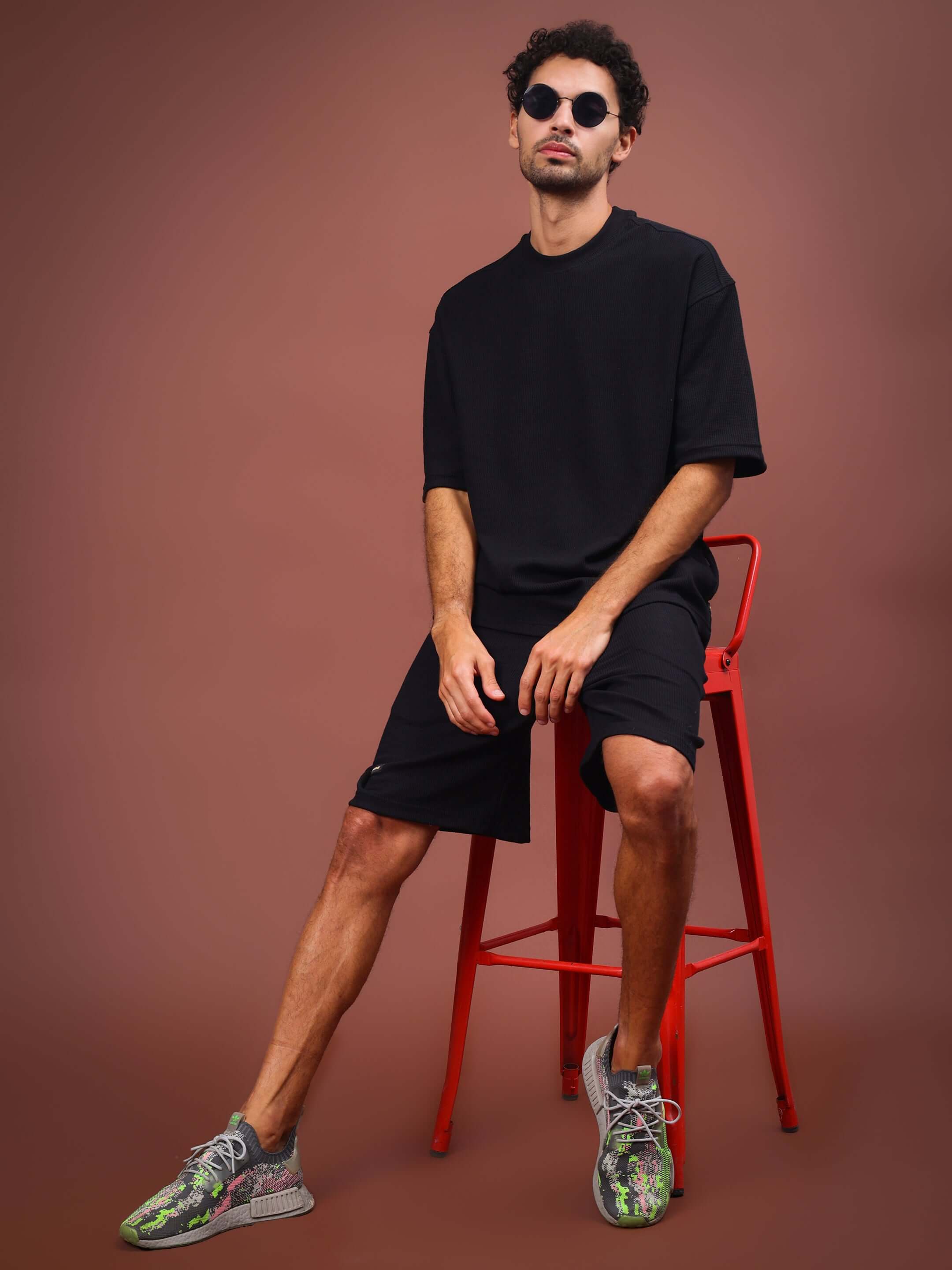Model wearing Highkey Solid Co-ord Set in black, featuring comfortable fit, seated on a red chair.