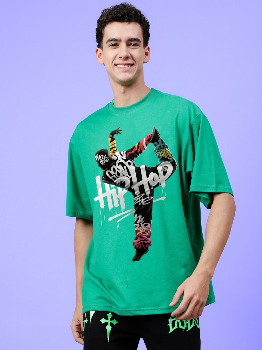 Man wearing HIP HOP OVER-SIZED T-SHIRT GREEN with graffiti design, expressing streetwear fashion against a purple background.