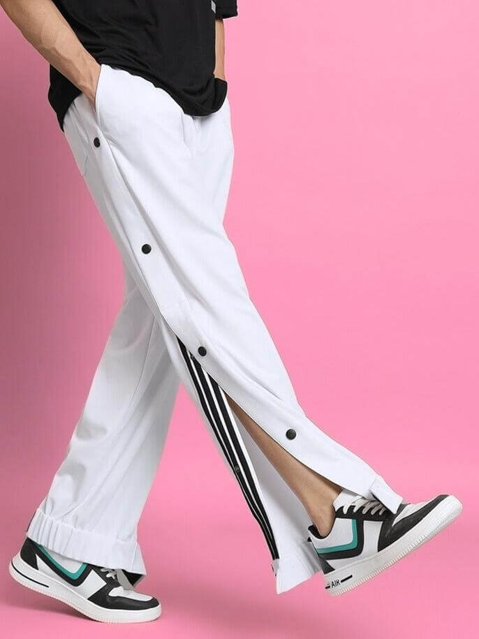 Person wearing white hip hop joggers with button details, styled with sneakers against a pink background.