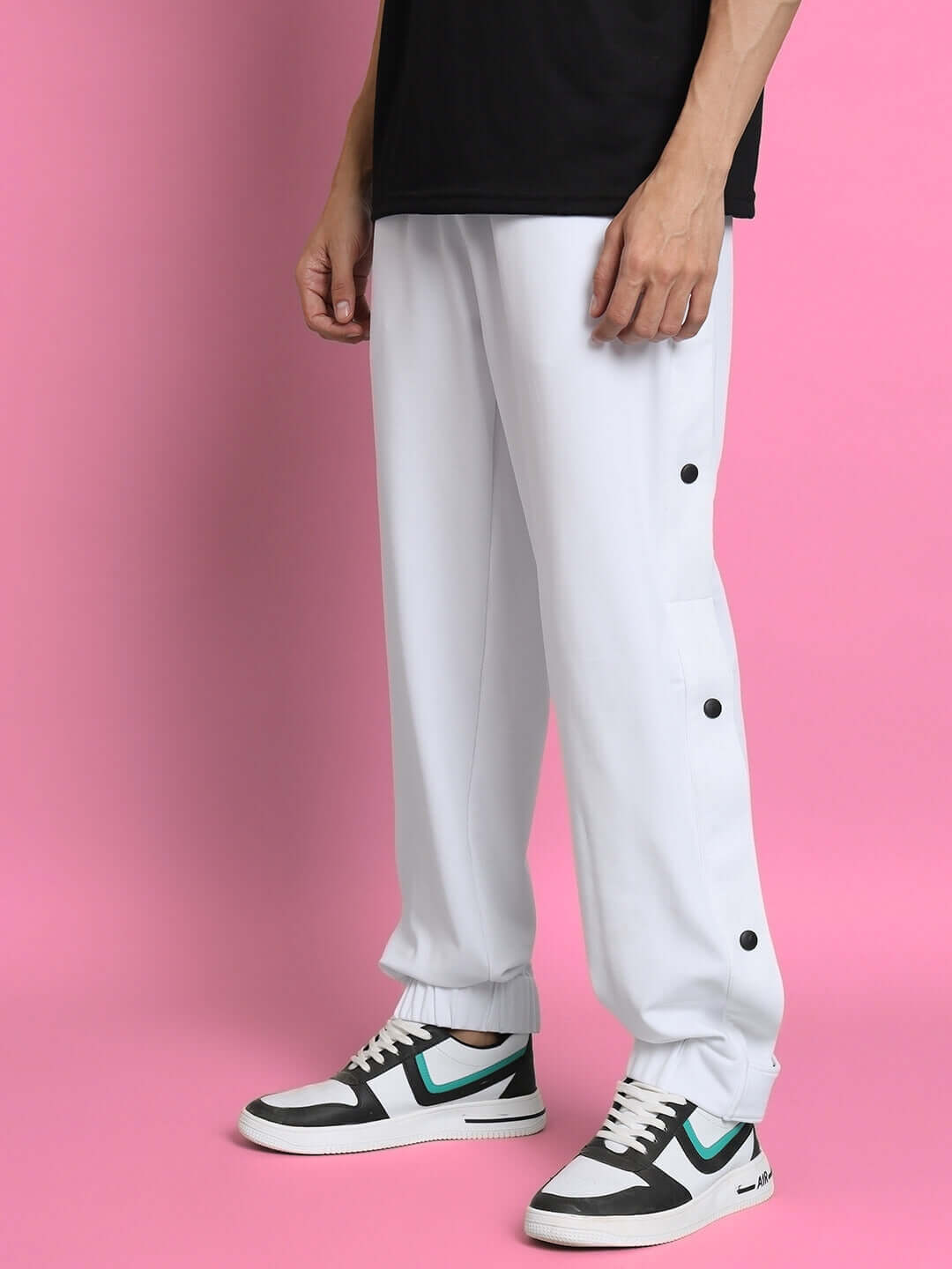 White hip hop joggers with button details worn by a model standing against a pink background.