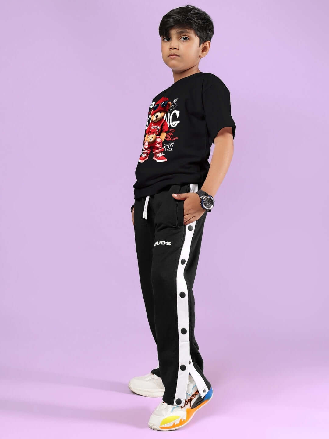 Young boy modeling black hip hop teddy co-ord set for boys & girls by DUDS, featuring a teddy graphic tee and side-striped pants.