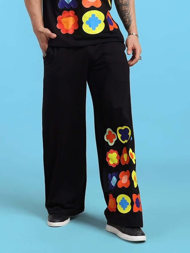 Colorful floral black joggers with vibrant patterns worn by a person on a light blue background.