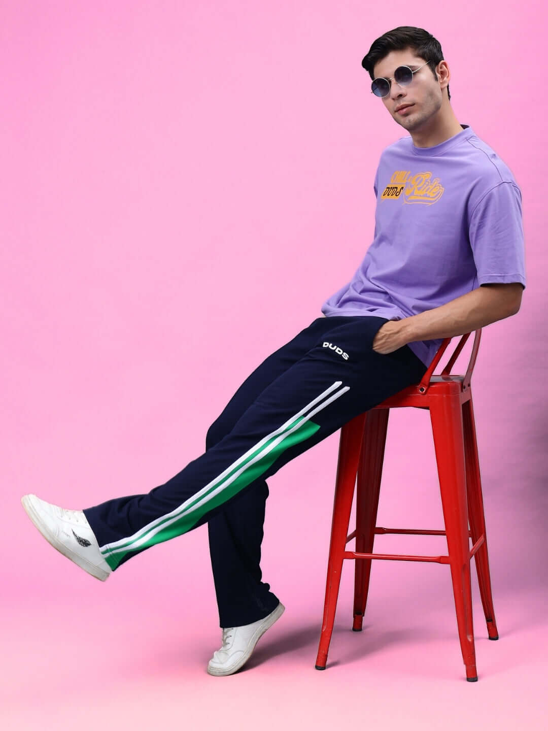 Model wearing Hoofer Contrast Joggers in navy blue-green, sitting on red stool with purple shirt, showcasing casual fashion style.
