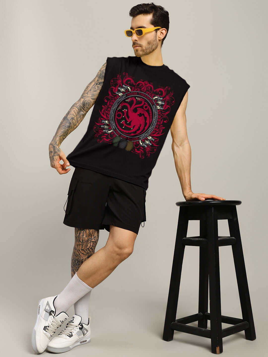 Man wearing HOUSE OF DRAGON PRINTED GYM T-SHIRT BLACK posing with a stool, showcasing dragon graphic and casual gym style.
