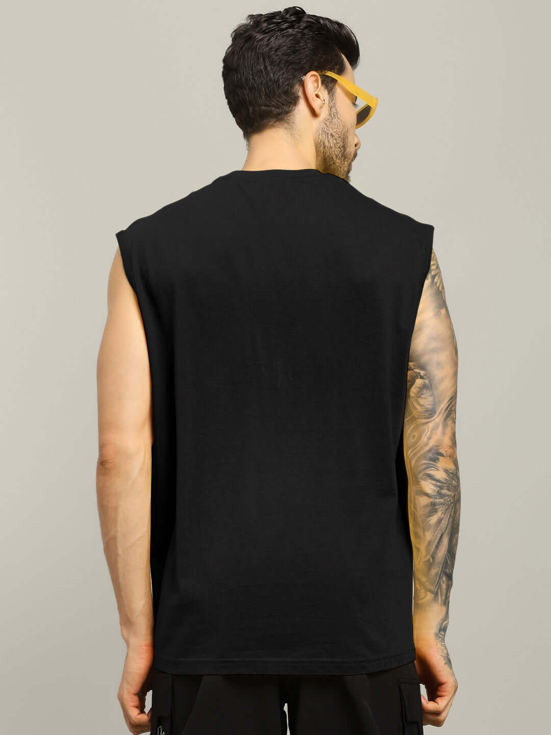 Back view of a man wearing a black House of Dragon printed gym t-shirt, showcasing tattoo on arm, styled with yellow sunglasses.