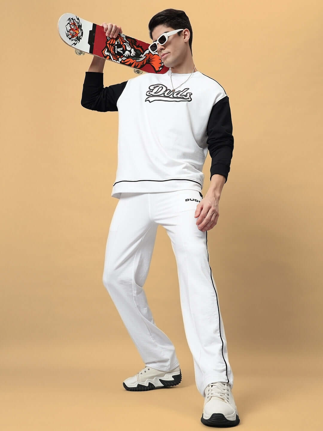 Model wearing HUNK oversized co-ord set in white with contrast panel joggers, holding a skateboard, showcasing relaxed fit fashion.