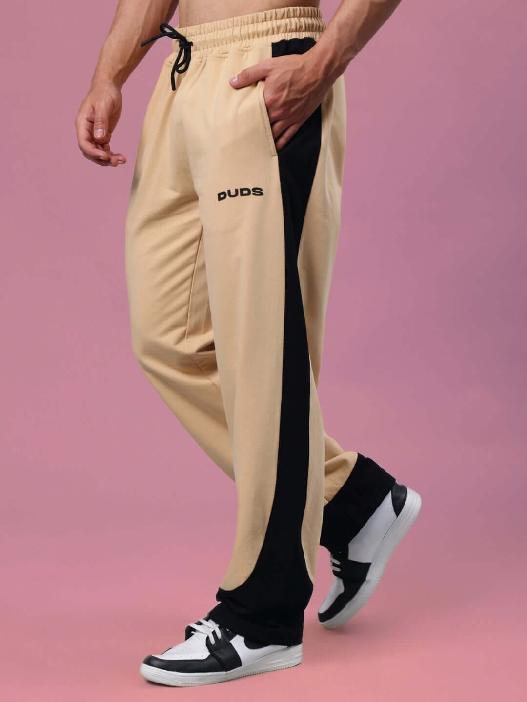 Men's HURTLE Baggy Joggers in beige-black by DUDS, made-to-order, customizable fit available, side view on pink background.