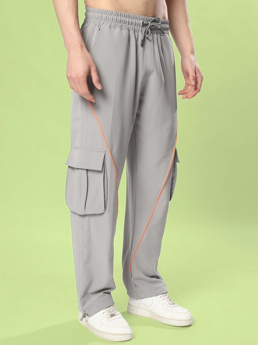 Grey cargo pants with neon orange accents, custom fit option available, shown on a male model with white sneakers, set against a green background.