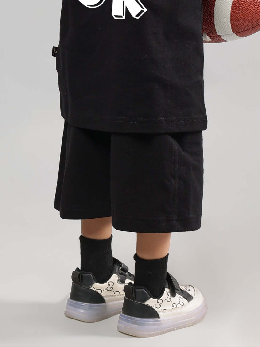 Child wearing I'M OK black shorts, designed for boys and girls, paired with sneakers; features customizable fit option. Made by DUDS.