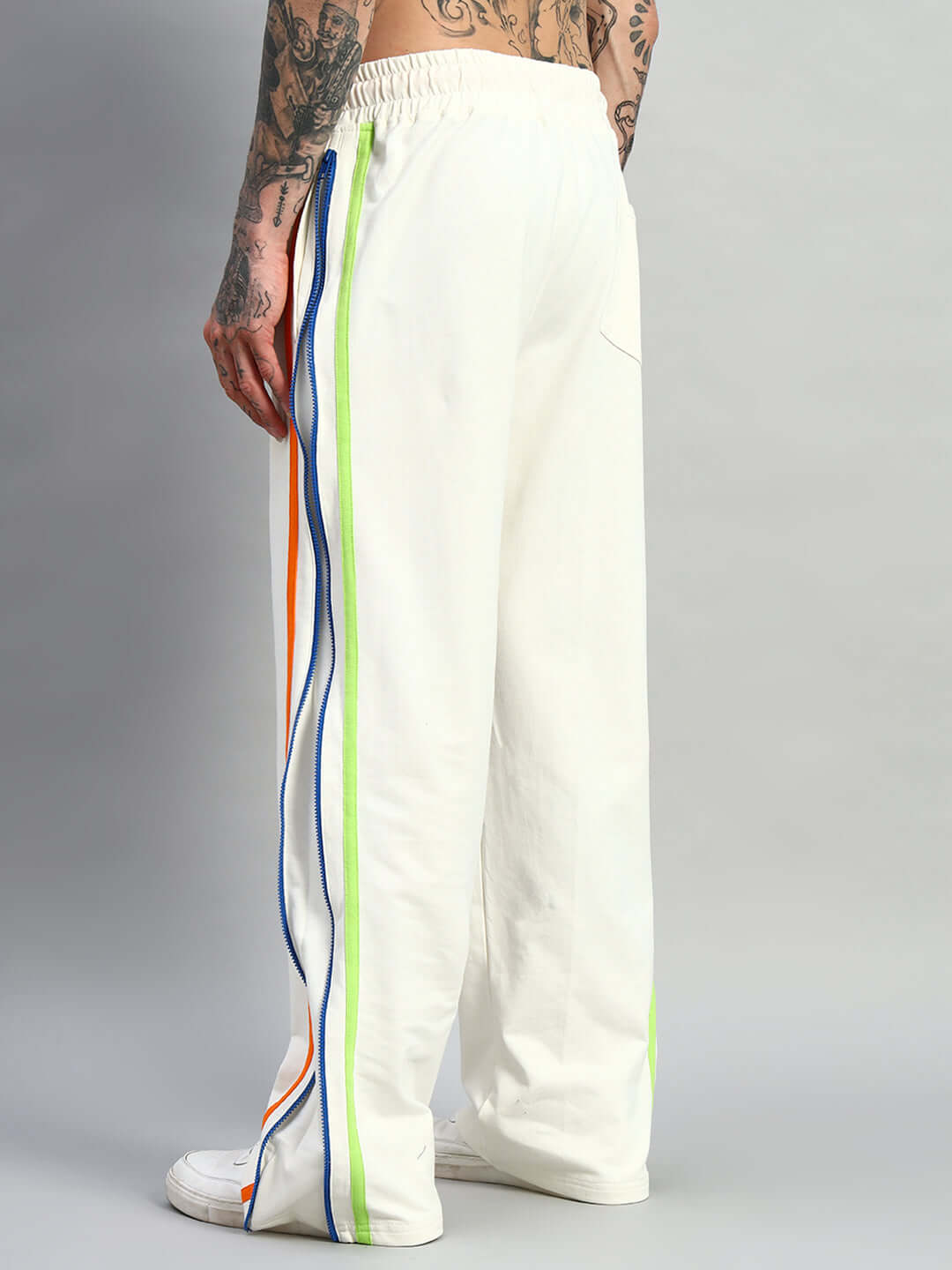 Back view of DUDS IMPERIAL Side Zipper Joggers in Off White with colorful side stripes, worn by a tattooed model.