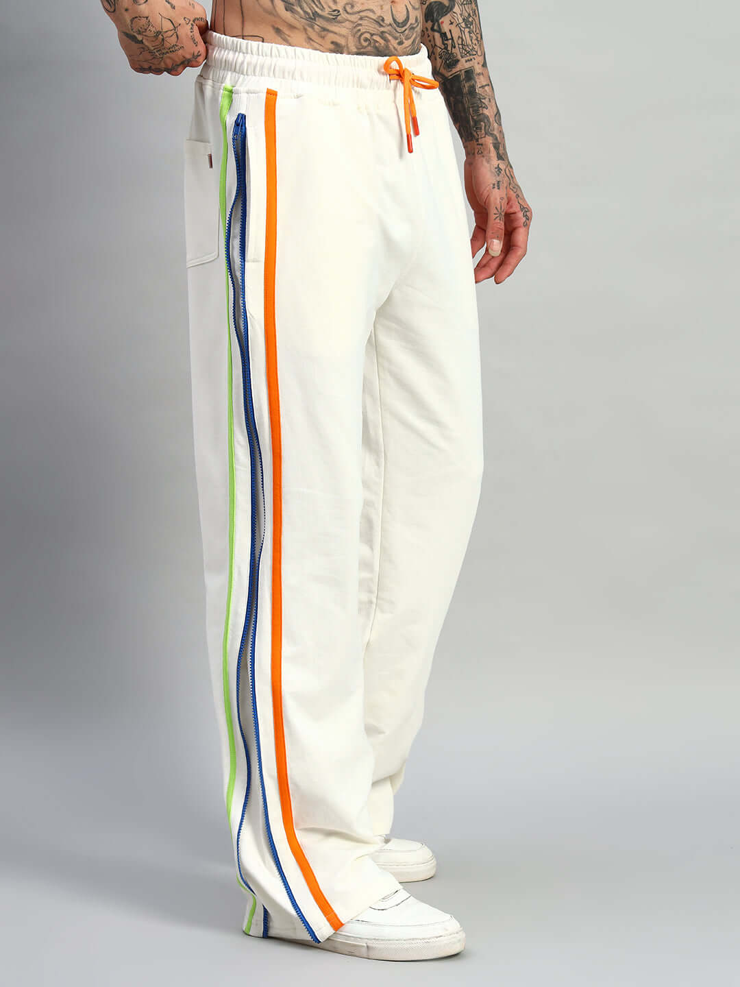 Off-white joggers with side zipper and colorful stripes, modeled by person with tattoos, showcasing DUDS customizable fashion.